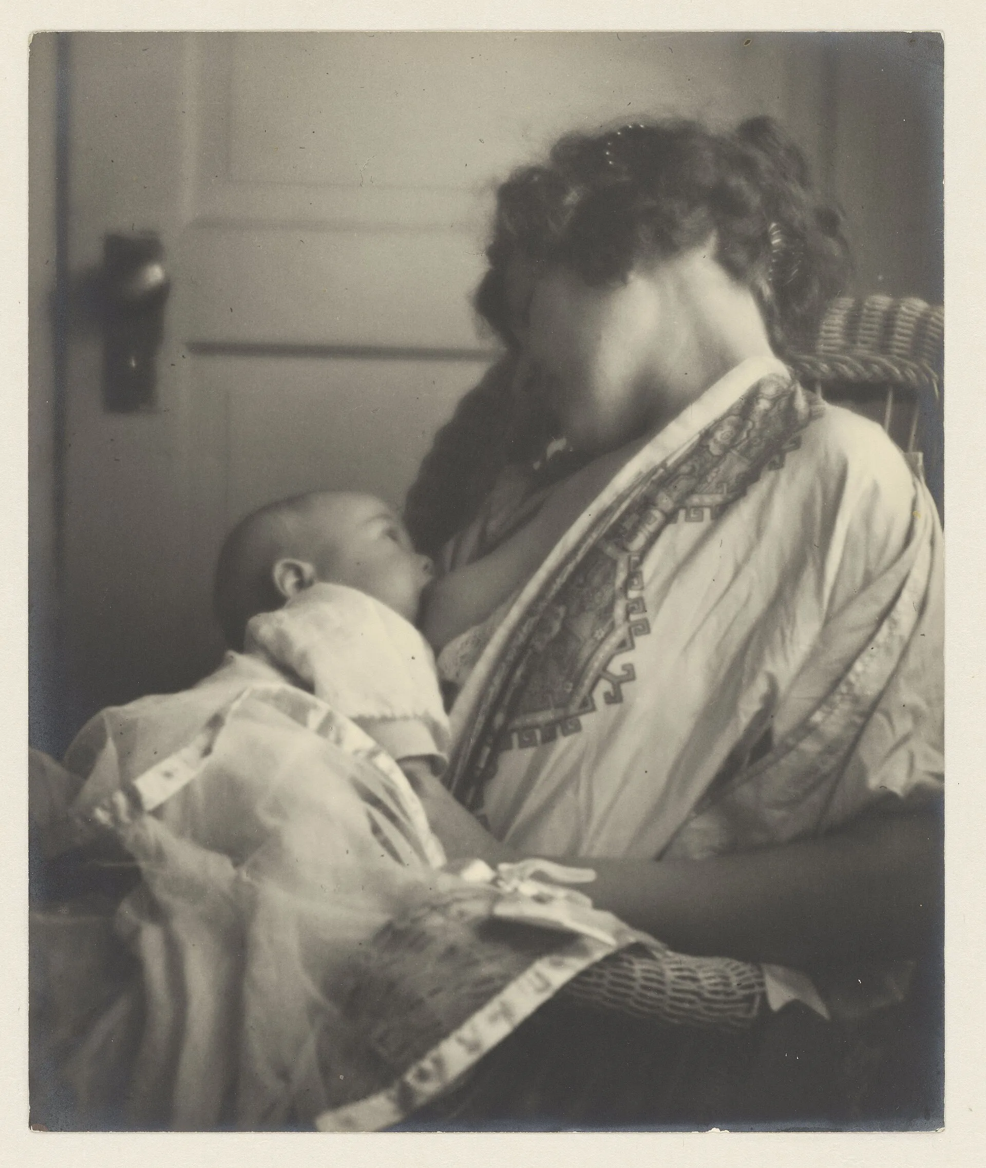 Fotografia de cerca de 1900, do acervo do Rijksmuseum: mãe sentada amamenta o bebê no colo, perto de uma porta.